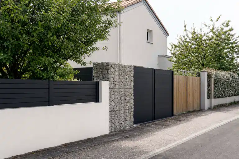 Portail noir moderne entre mur blanc et gabion
